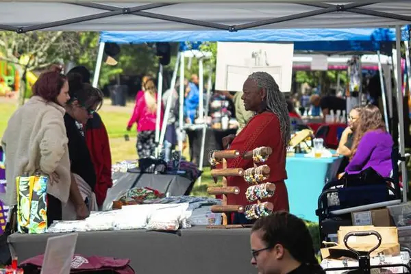 Black woman dressed in red smiling at two women looking at her handmade items at Mavuno