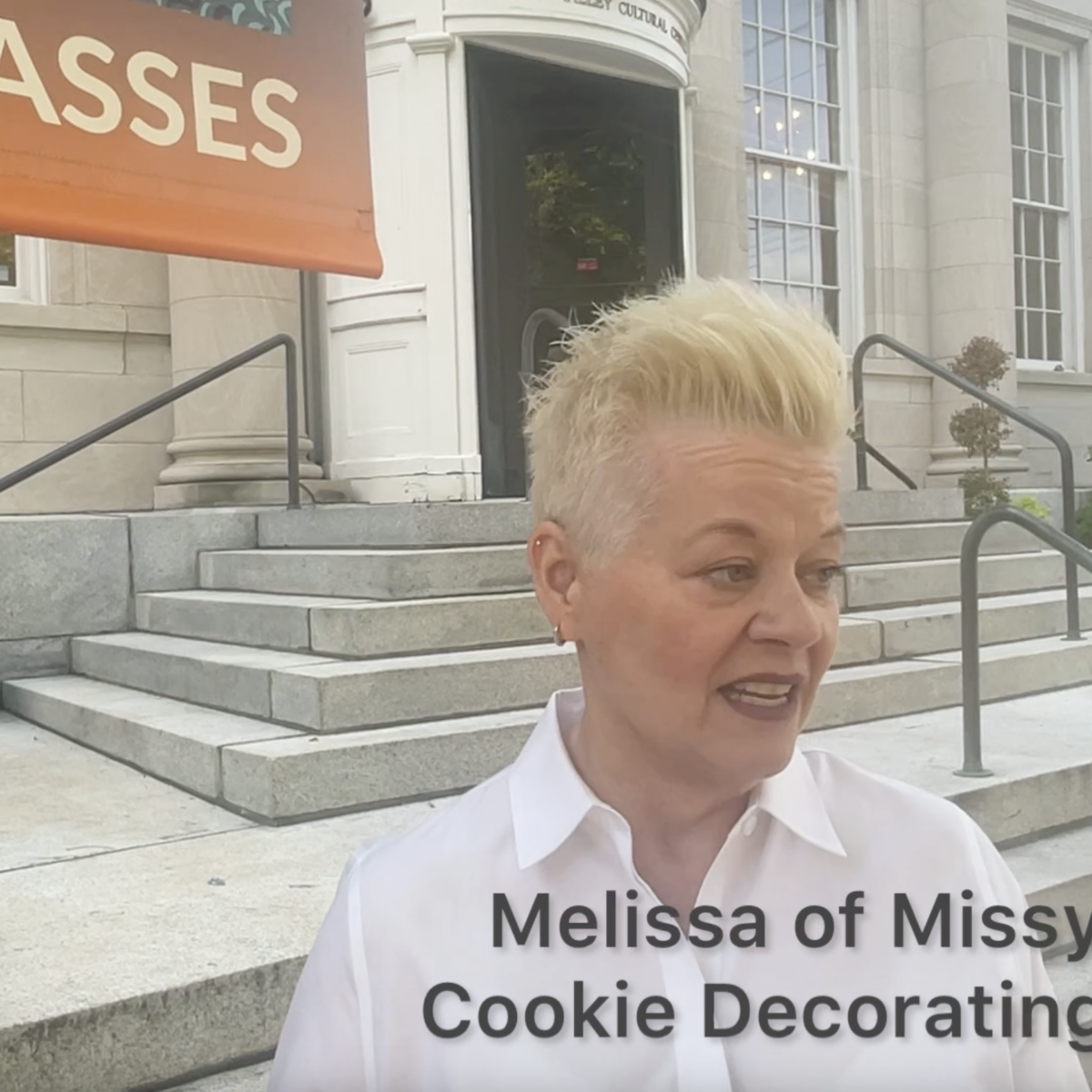 Missy from Missy's Morsels, a woman with bleach blonde short hair wearing a white button down shirt in front of the Sweetwater Center for the Arts entrance