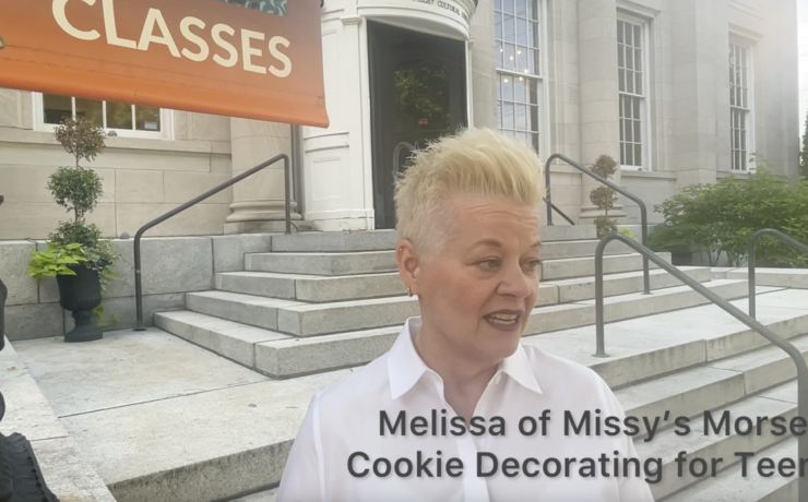 Missy from Missy's Morsels, a woman with bleach blonde short hair wearing a white button down shirt in front of the Sweetwater Center for the Arts entrance