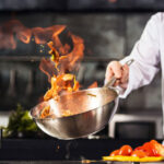Close up of chef's hand holding wok cooking with flame